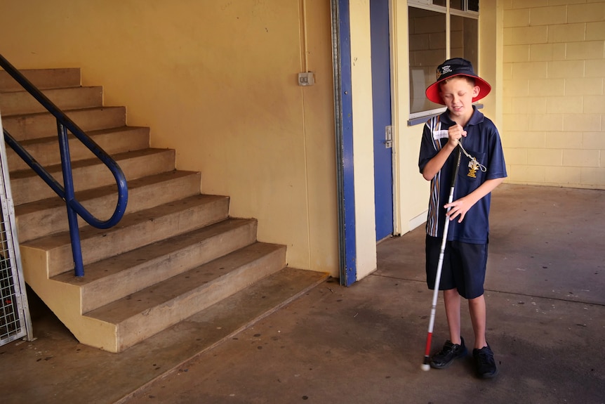 Young boy with white cane stands at the bottom of a flight of stairs