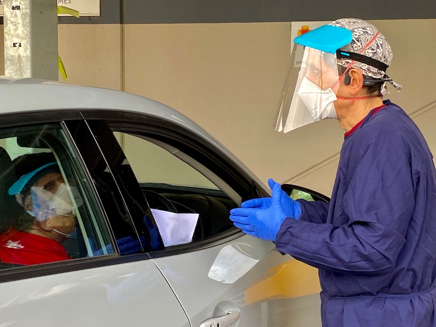 A person in PPE talks to a lady in a car, who is wearing a mask.