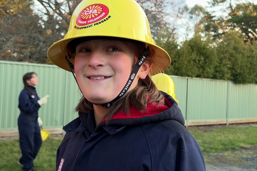 A girl in a yellow hard hat looks at the camera smiling