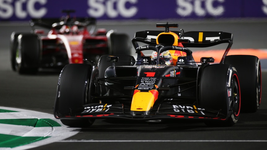 A blue F1 car leads a red F1 car through a corner.