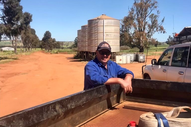 a man leans on the back of a ute with silos in the background