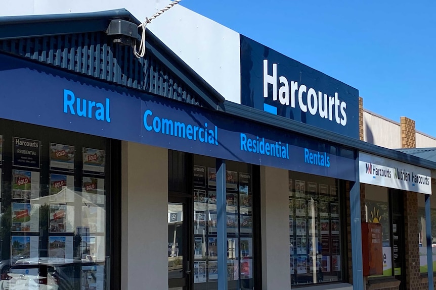 A blue sign with words listing the different types of real estate under the name "Harcourts" on a sunny day.