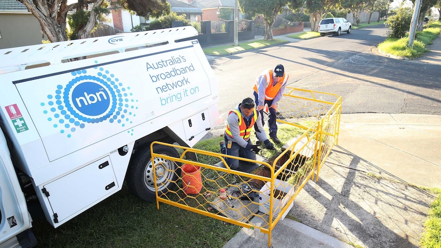 Two NBN workers kneel looking down a hole in the ground with a truck behind them on a suburban street