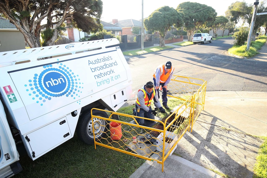 Two NBN workers in fluoro vests install broadband around a pit on a suburban street