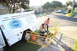 Two men next to an NBN cable pit and an NBN truck.