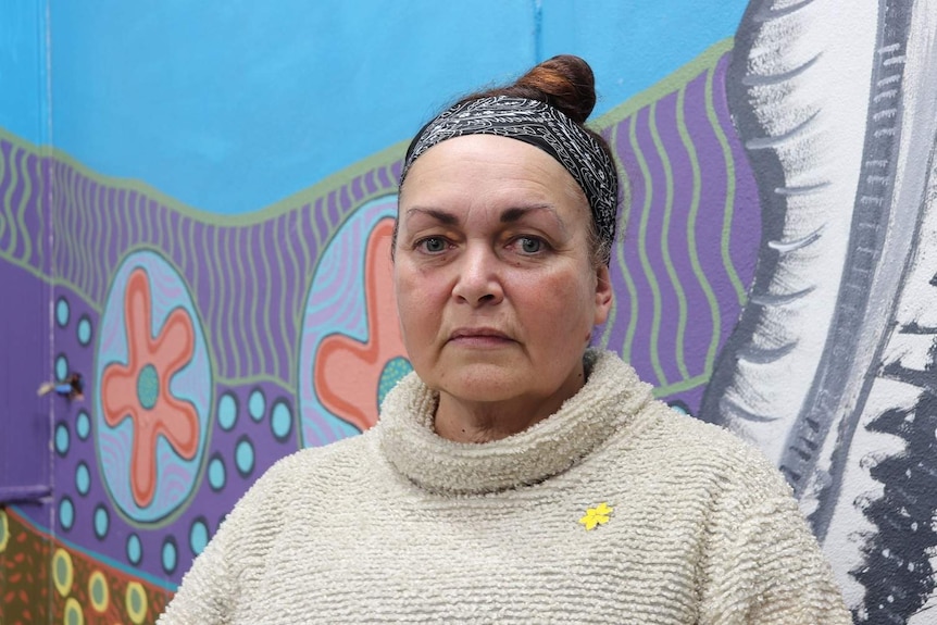 A portrait shot of Julie Perkins, chairwoman of Gurehlgam Corporation, in front of  wall featuring indigenous art.