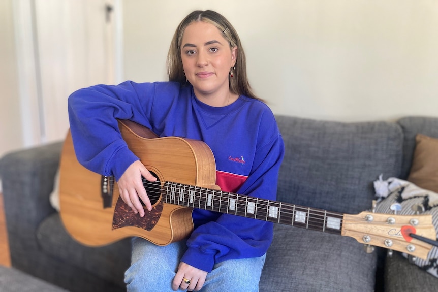 A woman sits on a couch with a guitar.