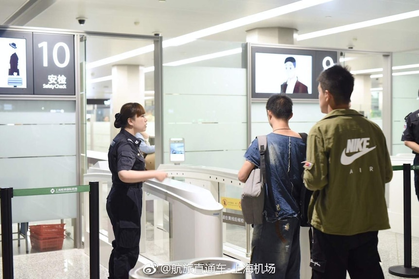 An airport staff member stands by as a passenger through the facial recognition check-in