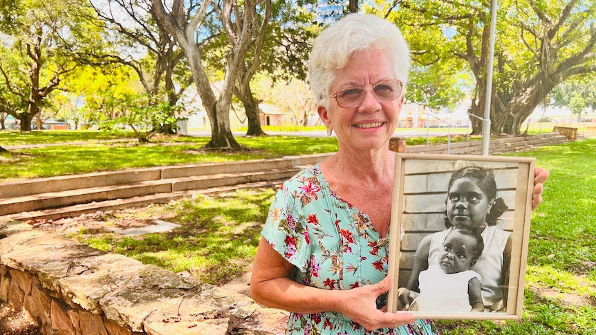 Lady sits in a park with a photo of her young sister in a photo frame