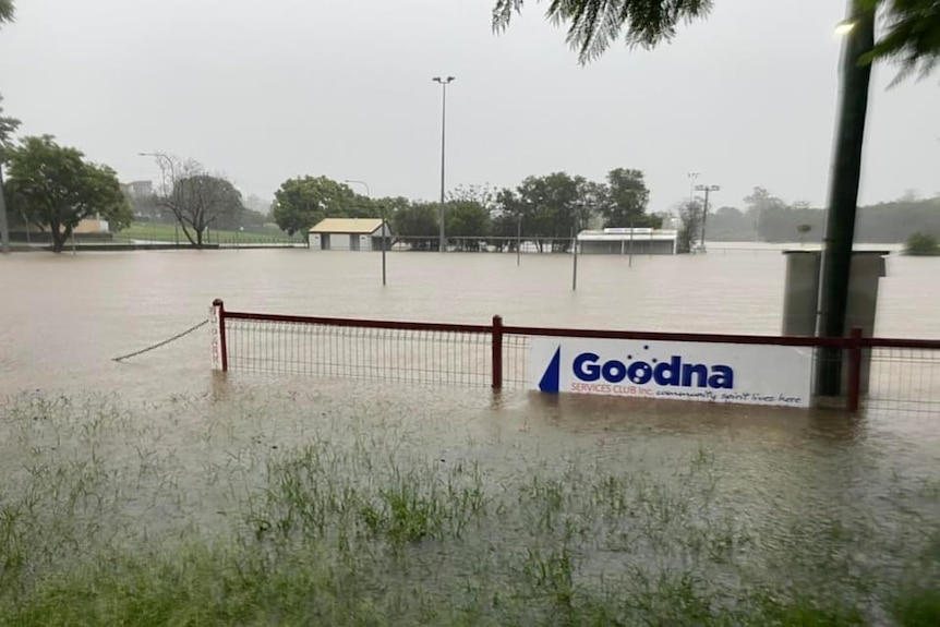 A flooded field with a sign on a fence still visible that reads "Goodna Services Club"