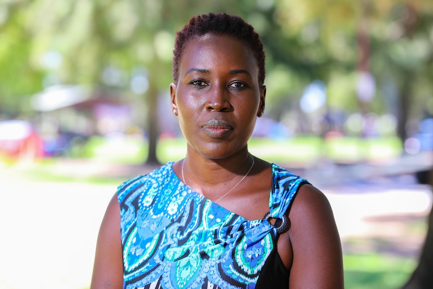 A woman in a blue dress standing in a park, looking at the camera.