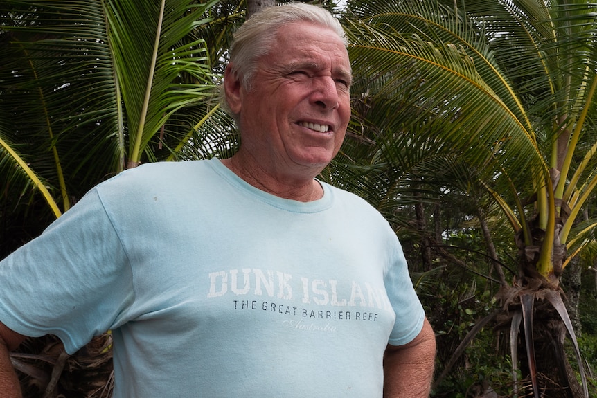 Man standing on beach in front of palm trees looking out to sea.