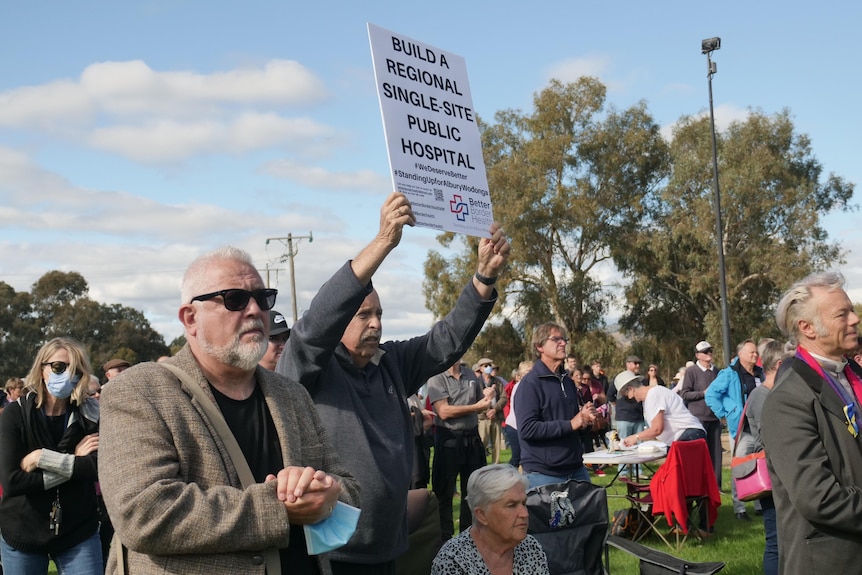 A man holds up a sign at a rally for a single-site hospital to be built. 