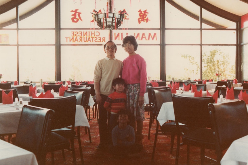 A family poses for a photo standing in the middle of a dining room of a Chinese restaurant