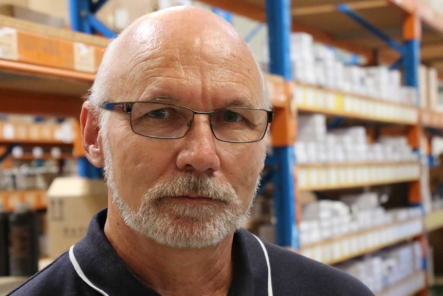 A man with glasses wearing a blue polo shirt stands in a warehouse.