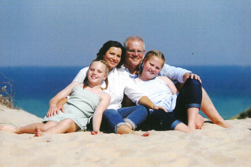 Prime Minister Scott Morrison, Jenny Morrison, and the couple's children Abbey and Lily sitting on the sand at a beach.