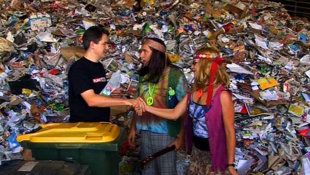 Man shakes hands with woman beside wheelie bin, in front of large pile of rubbish