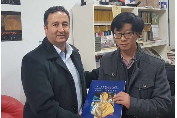 Two men in office hold book called Australia's First Parliament with bookshelves in background