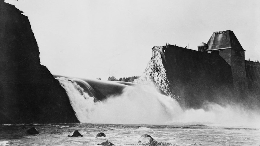 A black and white image of a dam that has been blown apart.