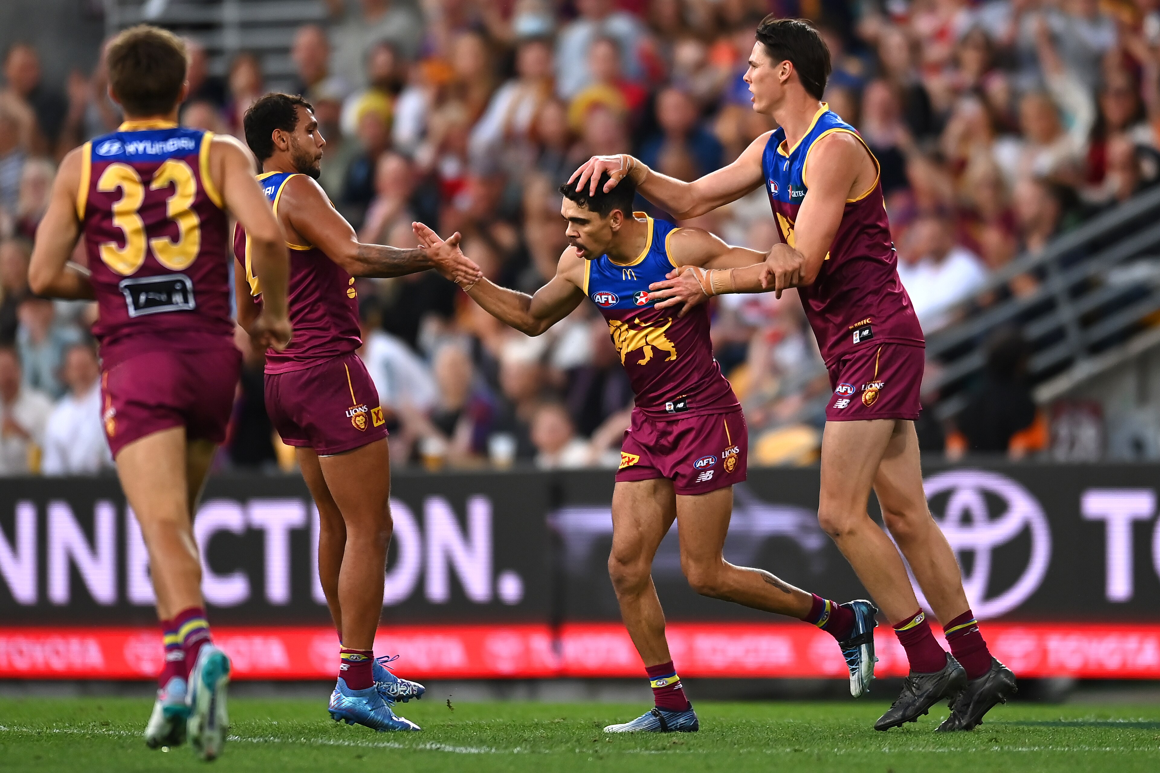 Brisbane AFL players high-five and pat a teammate on the shoulder as he runs back after kicking a goal.