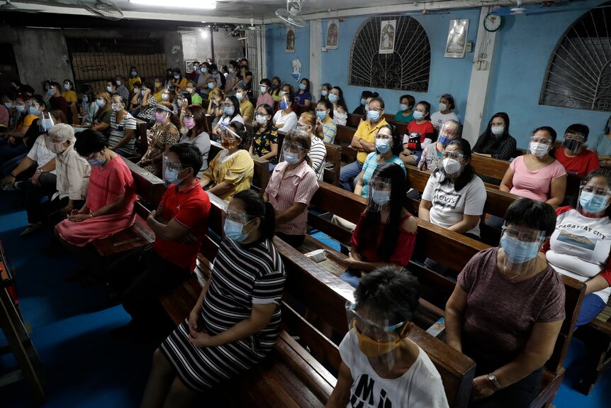 Residents wearing face masks sit apart during a church service
