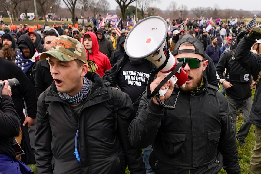 Proud Boys members Zachary Rehl (left) and Ethan Nordean holding a megaphone (right) walk toward the US Capitol.