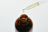 A liquid dropper is pulled out of a small brown glass bottle. 