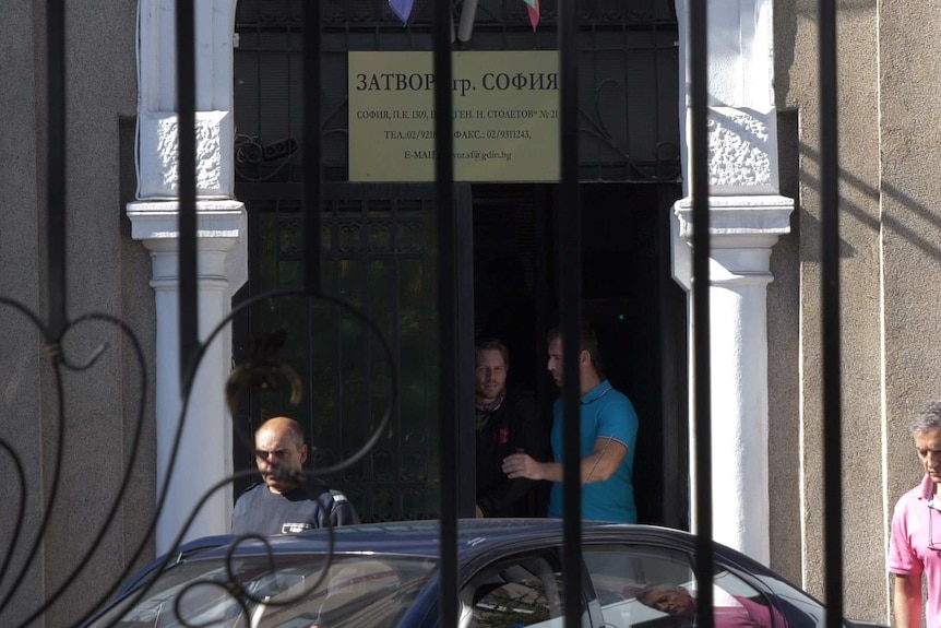 Jock Palfreeman is led outside a door towards a waiting car while men stand around.