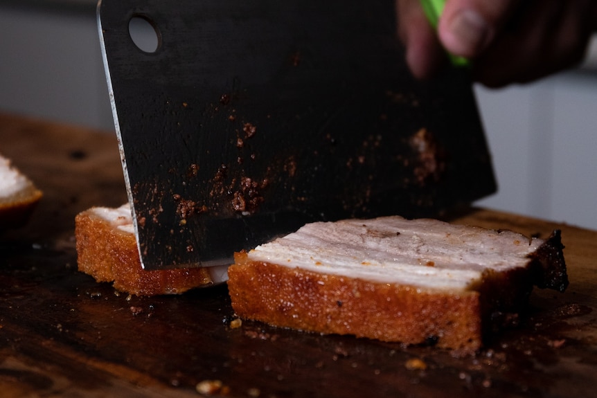 A piece of pork meat being chopped by a knife.