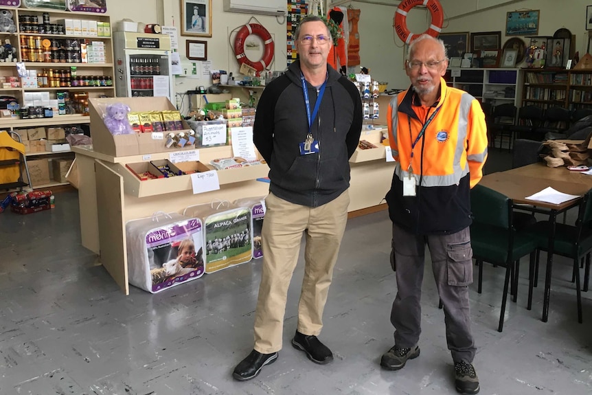 Two men stand inside a sparsely stocked shop.