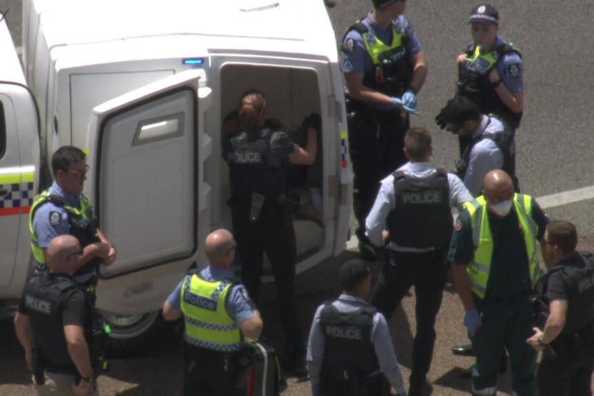 Officers surround a police wagon on a Perth freeway as a man is ushered inside.