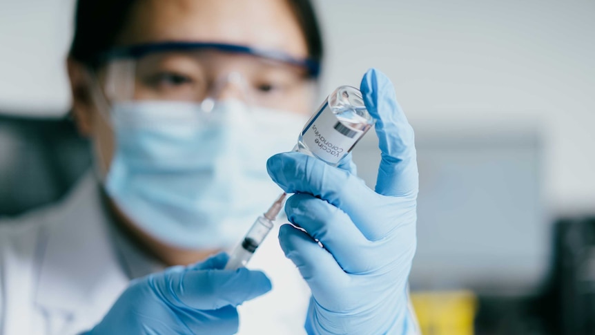 A medical worker in full PPE fills a syringe with COVID-19 vaccine.