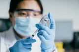 A medical worker in full PPE fills a syringe with COVID-19 vaccine.