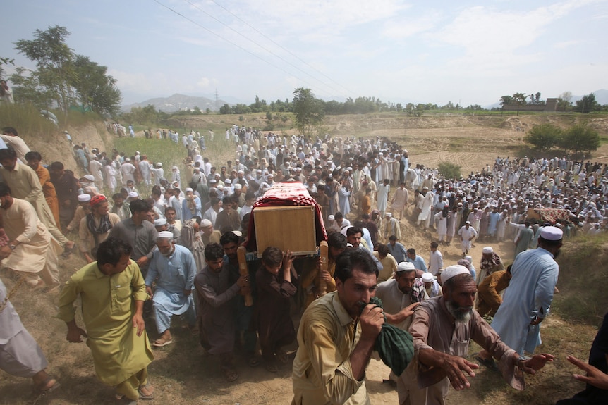 A crowd at a funeral carrying a coffin. 