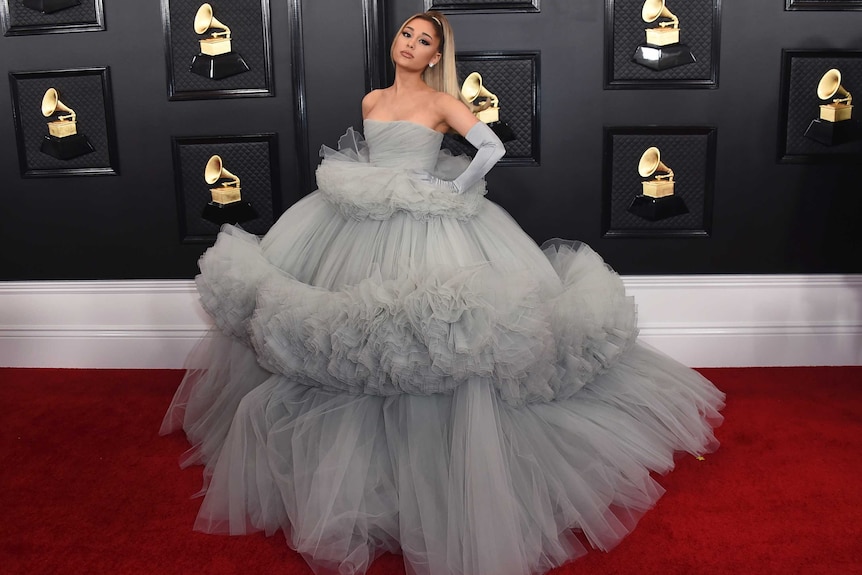 Pop star Ariana Grande poses on the Grammys red carpet in a large grey gown and gloves