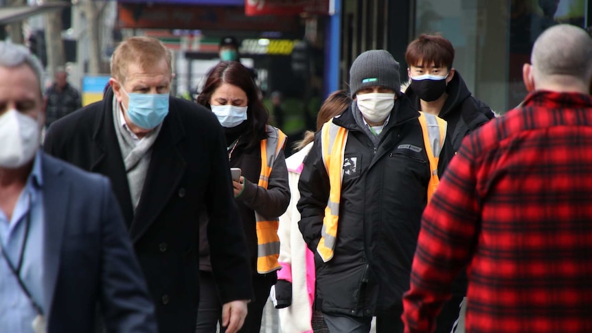 People walk down a busy section of Swanston Street in Melbourne, all wearing face masks.