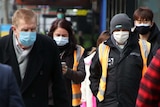 People walk down a busy section of Swanston Street in Melbourne, all wearing face masks.