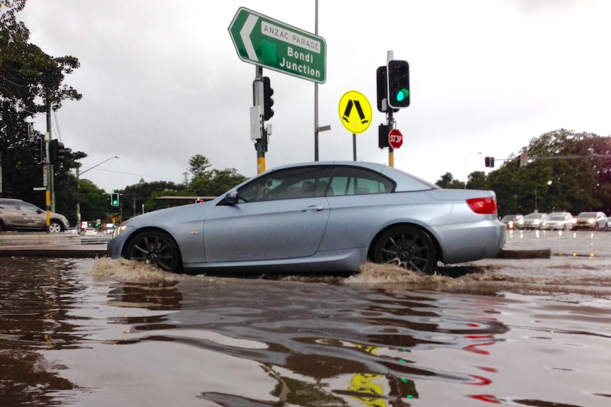 A car drives through low floodwater at the intersection of Anzac Pde and Cleveland St at Moorre Park, Sydney, August 3, 2016