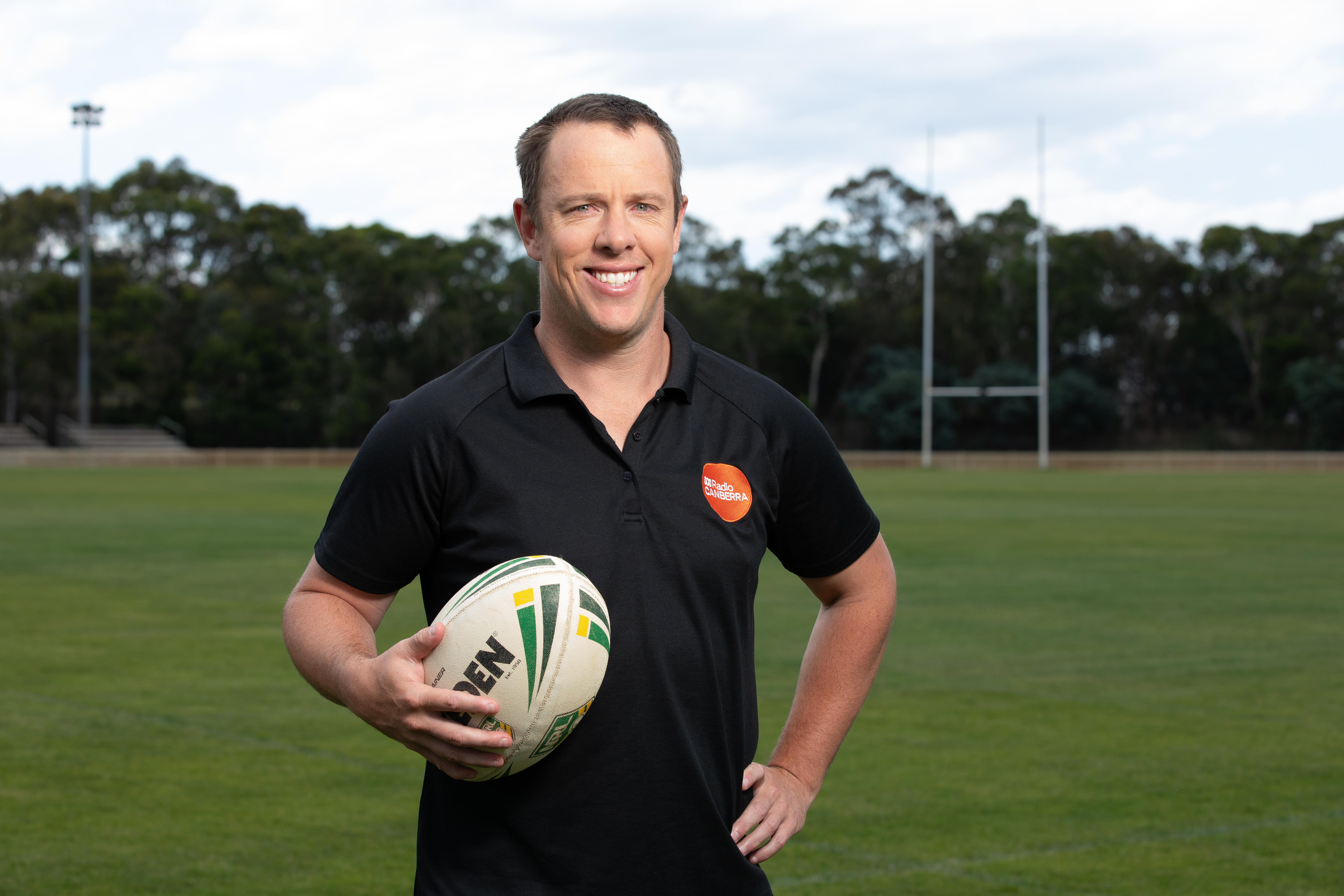 Sam Williams standing on a footy oval, holding a football.
