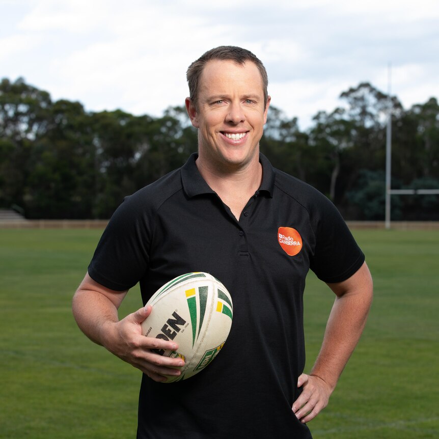 Sam Williams standing on a footy oval, holding a football.