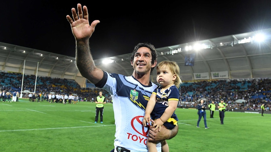 Johnathan waves to the crowd as he carries one of his children on a lap of honour in Robina.