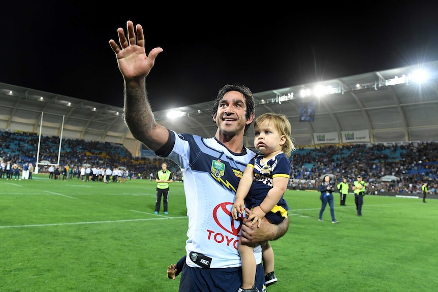 Johnathan waves to the crowd as he carries one of his children on a lap of honour in Robina.