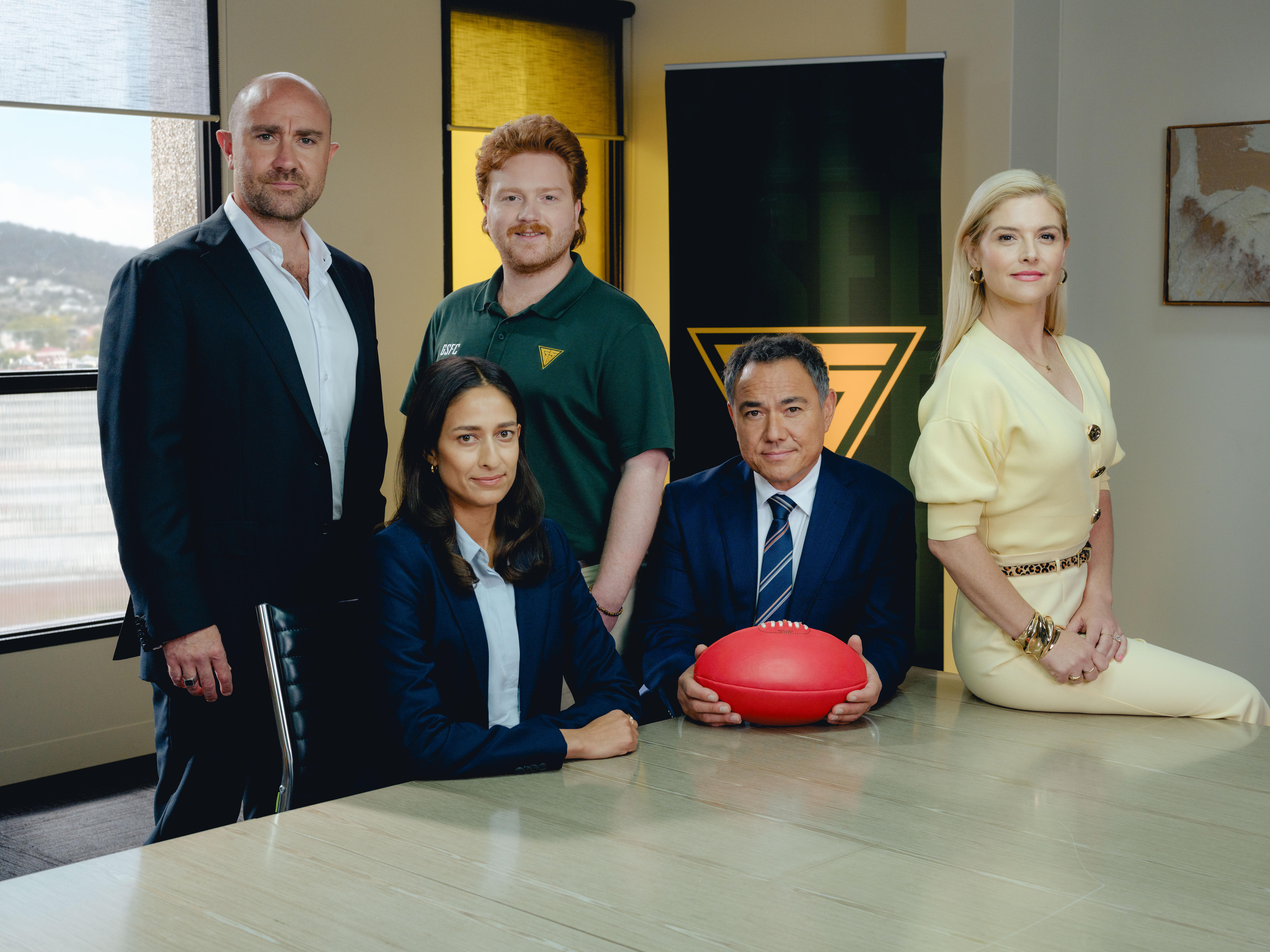 A group of actors on the sert of Ground Up post as a group around a board table. 