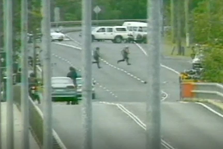 A long shot of officers in protective gear running across a road.  Police cars are blocking the road in the background.