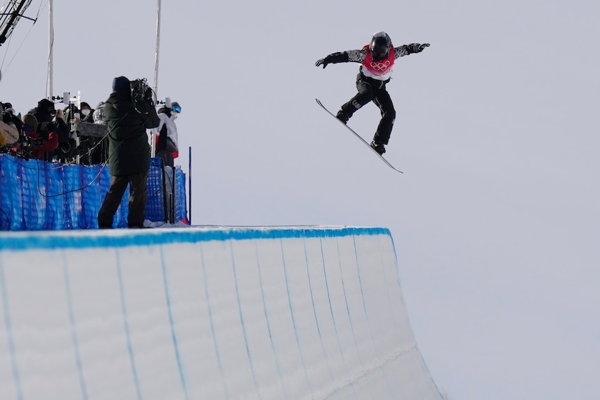 A man flies high above a halfpipe on a snowboard.