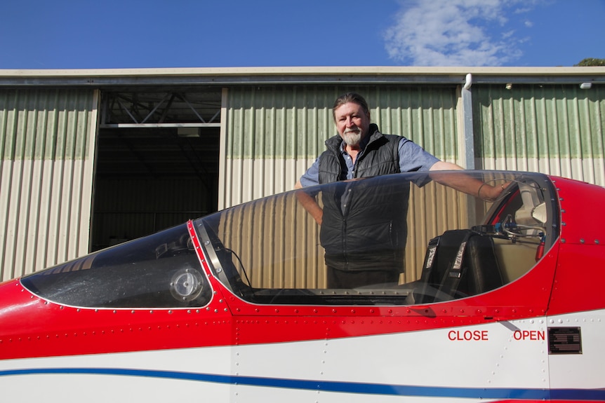 A man leaning against the cockpit of his homemade red jet.
