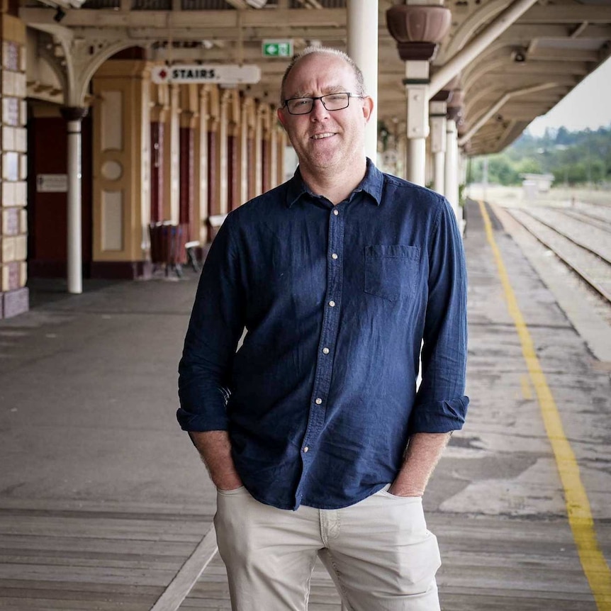 David Iliffe leaning against a column at a train station.