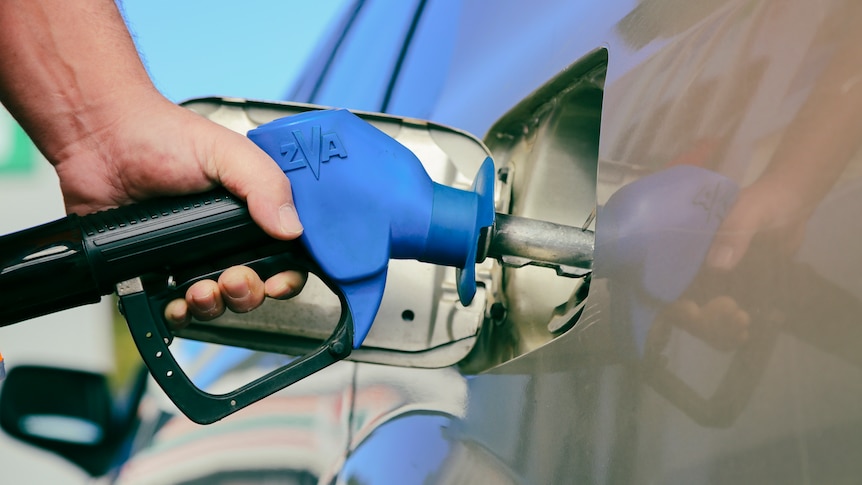 A man holds a petrol bowser while filling up his car.