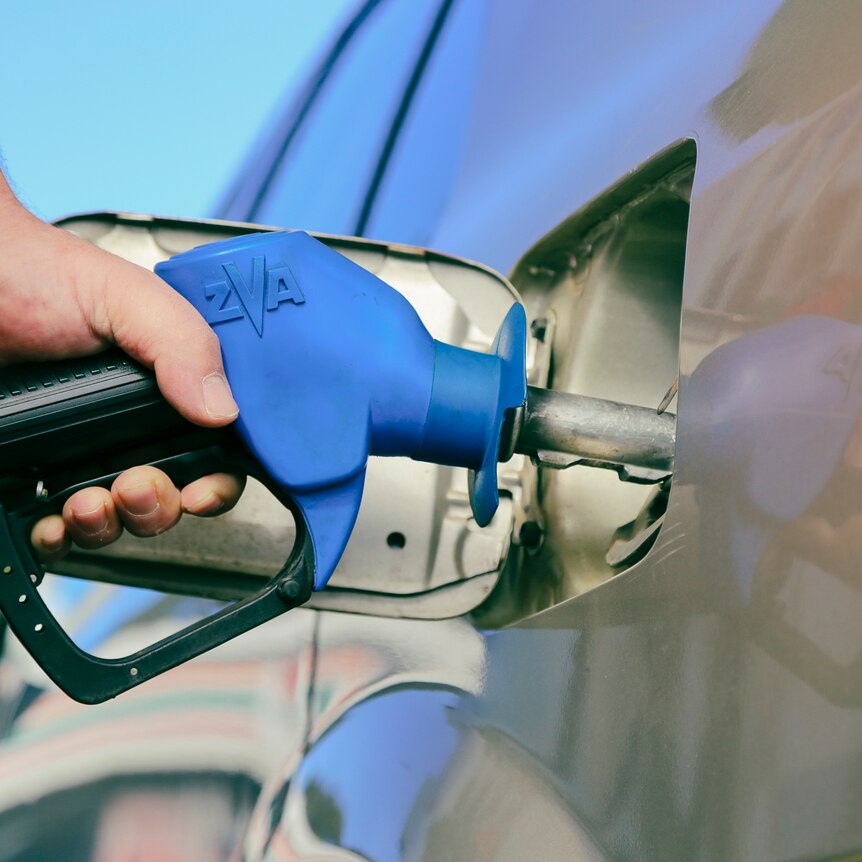 A man holds a petrol bowser while filling up his car.