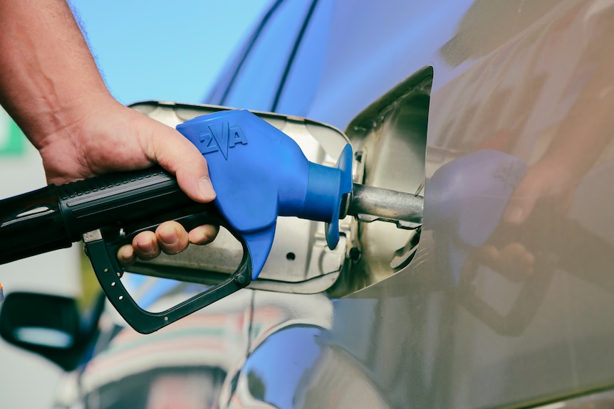 A man holds a petrol bowser while filling up his car.